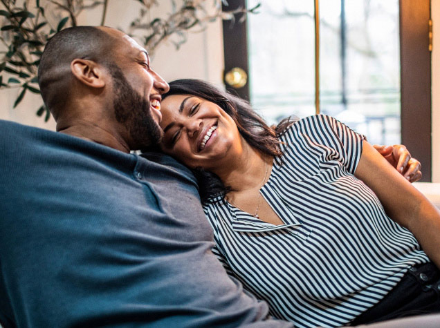A man is smiling and embracing a smiling woman with his left arm.